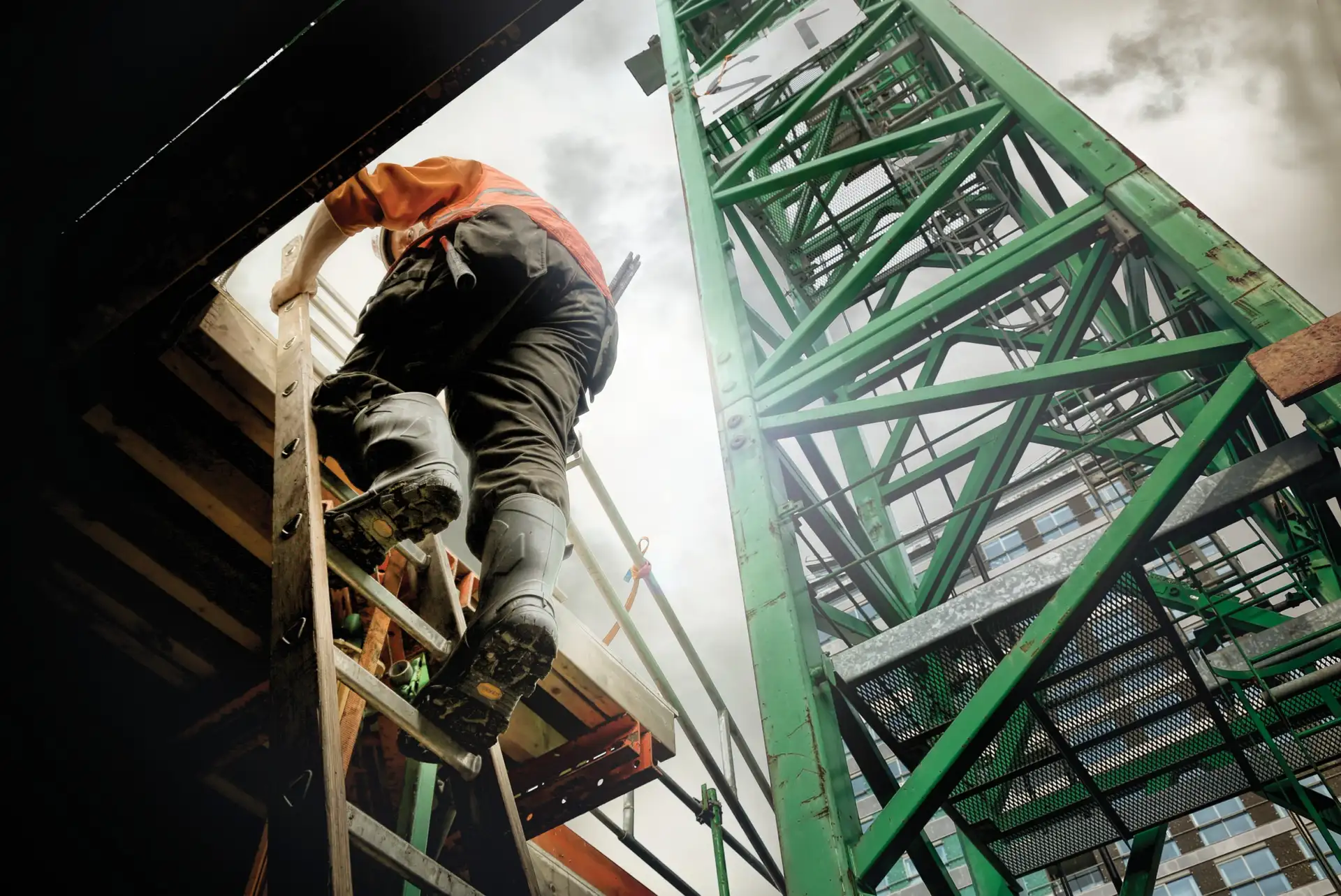 Indutry worker climbs up a ladder, in front of a green crane